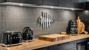 Une cuisine moderne équipée d’une hotte en acier inoxydable, d’une machine à café, d’un grille-pain et d’un porte-couteaux fixé au mur.
