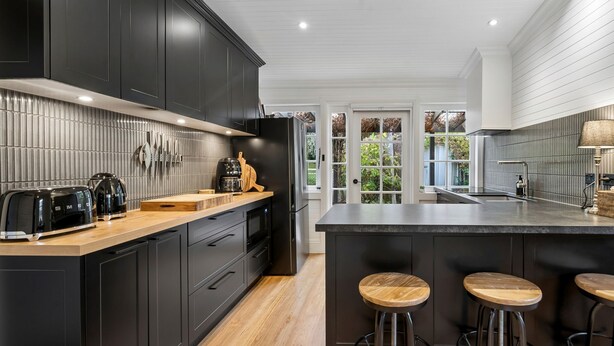 Une cuisine moderne avec des meubles de couleur sombre, un plan de travail en bois et un grand îlot central doté de tabourets.