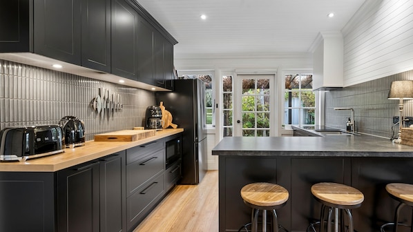 A modern kitchen with dark cabinetry, a wooden countertop, and a large island with stools. - Brixton Cottage in Katoomba (Katoomba)