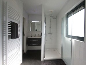 Ein modernes Badezimmer mit Duschkabine aus Glas, einem großen Spiegel und einem dunklen Waschtisch.