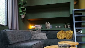Una sala de estar moderna con un sofá gris, una mesa de centro de madera y una pared verde decorada con objetos.
