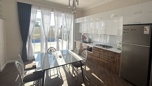 A modern kitchen with white cabinets, a stainless steel refrigerator, and a dining area with a glass table and chairs. - Spacious 4-bedroom home with air conditioning in beautiful Baku near Miami Beach (Baku)