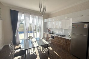 Una cocina moderna con armarios blancos, un refrigerador de acero inoxidable y un comedor con una mesa y sillas de vidrio.