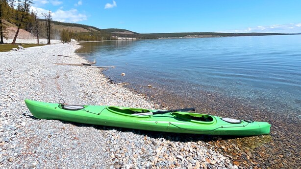 Un kayak verde sobre una orilla pedregosa a orillas de un lago tranquilo, con cielos despejados.