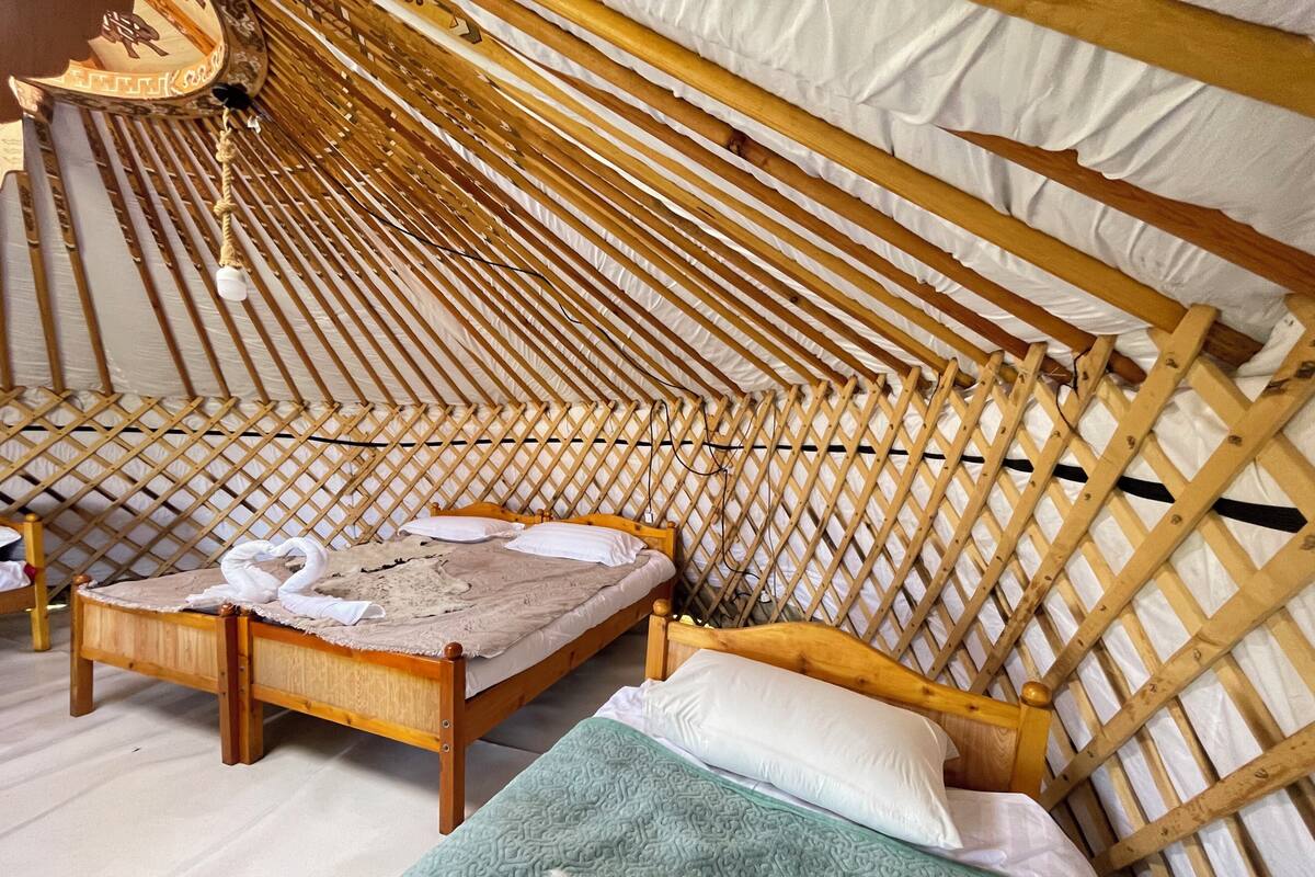 Uma tenda aconchegante com estrutura de madeira, uma cama, almofadas e um cobertor.