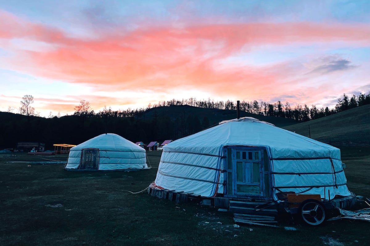 Yurts num campo gramado sob um céu ao pôr do sol.