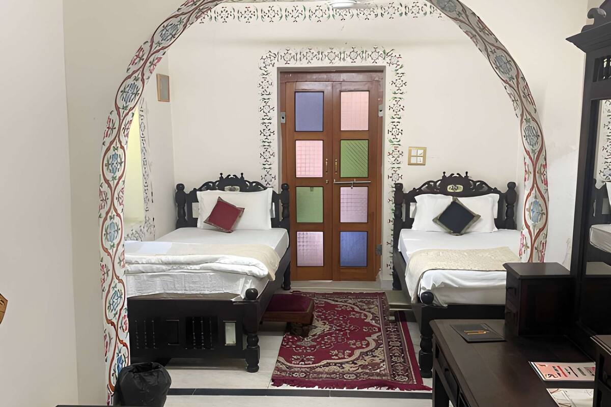 Une chambre avec deux lits, un bureau, une chaise, un tapis et un portail décoré.