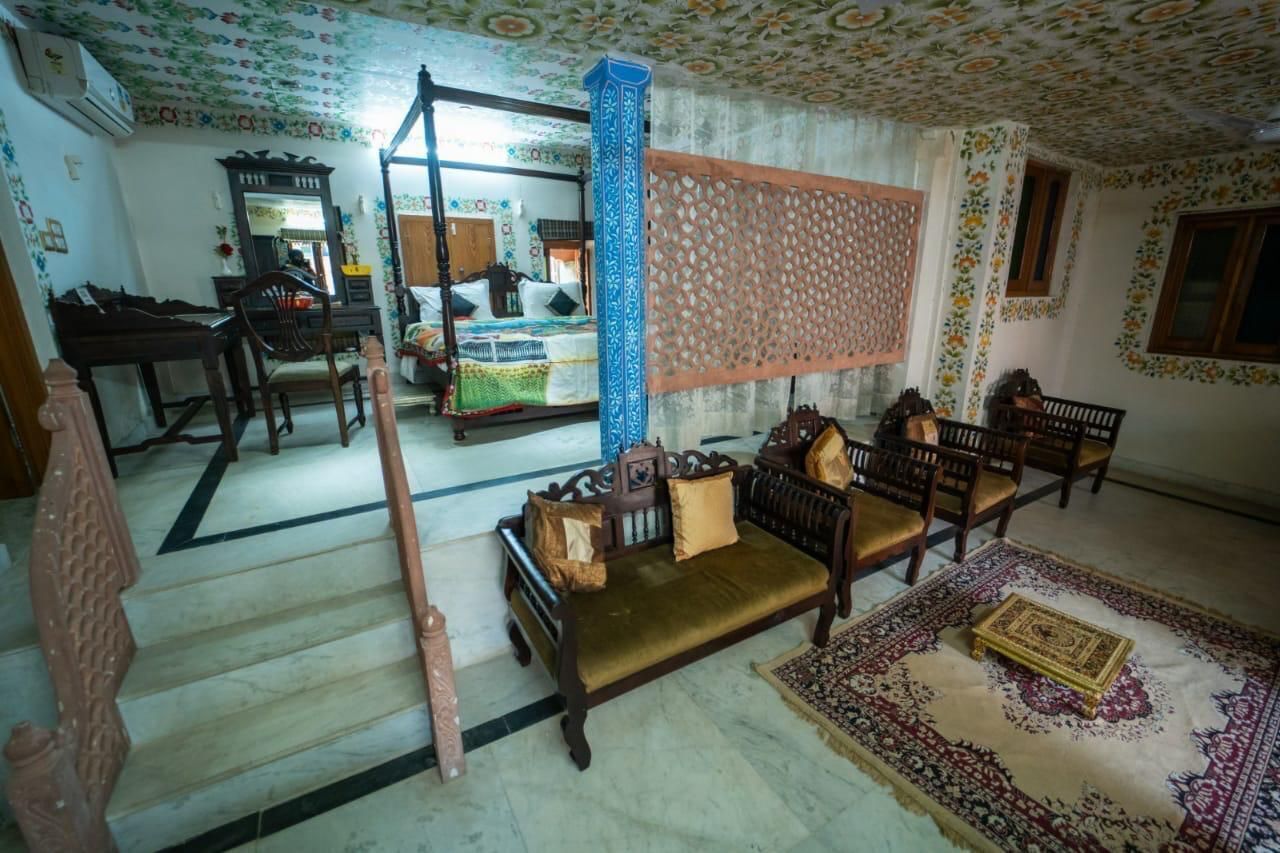 A room with a bed, a sofa, a wooden chair, a table, and a patterned wall.