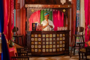 Una tradicional tienda de té india con un mostrador de madera, baldosas coloridas y un hombre detrás del mostrador.