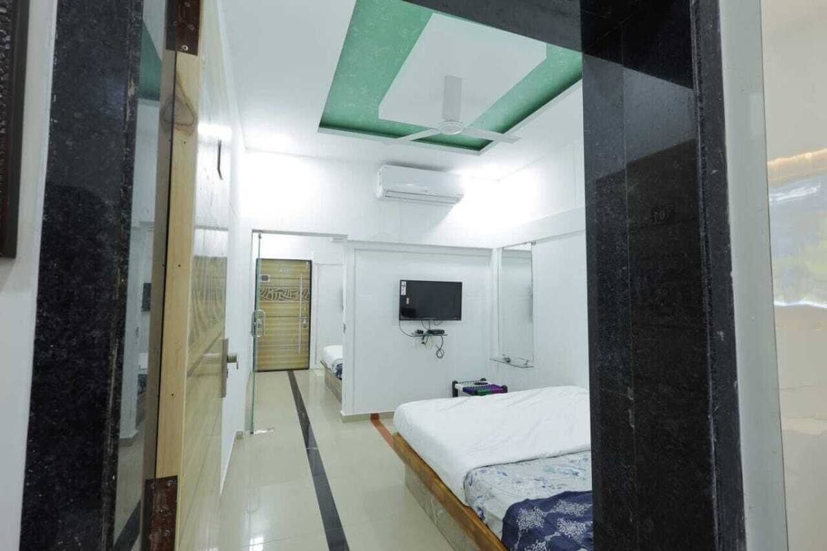 Una habitación de hotel con cama, televisor, ventilador de techo y aire acondicionado.