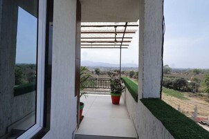 A balcony with a view of a rural landscape, a potted plant, and a pergola structure.