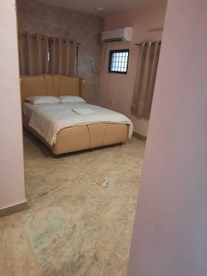 A bedroom with a bed, curtains, an air conditioning unit, and a window. - Skyry Hotels Alapakkam (Chennai)
