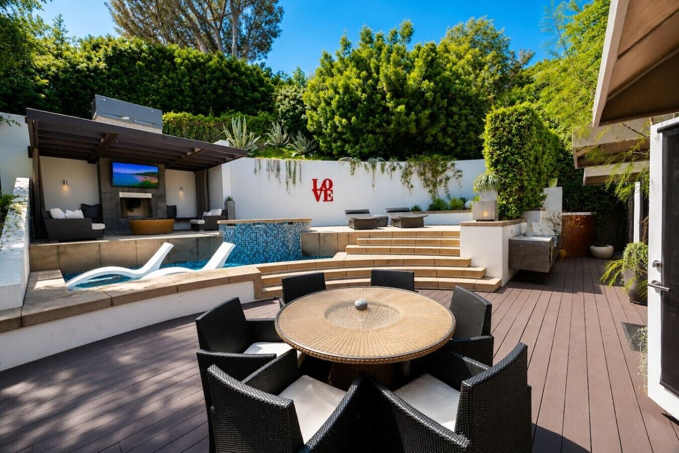 An outdoor patio with a pool, lounge chairs, a round table, and a 'LOVE' sign on the wall.