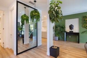 Ein modernes Interieur mit einem großen Spiegel, hängenden Pflanzen, einem Blumentopfbaum und einer Buddha-Statue auf einer Konsole.