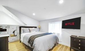 Ein Schlafzimmer mit einem Bett, einem an der Wand befestigten Fernseher, einem Kleiderschrank und einem Schreibtisch.