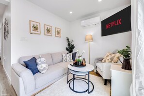 Ein modernes Wohnzimmer mit einer Couch, einem Couchtisch und einem Flachbildfernseher, der 'NETFLIX' anzeigt.
