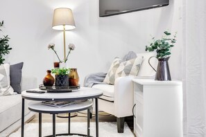 Ein modernes Wohnzimmer mit einem runden Couchtisch, einer Stehlampe, einer Couch und einem an der Wand befestigten Fernseher.