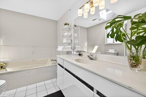 Ein modernes Badezimmer mit einer Badewanne, zwei Waschbecken, einem großen Spiegel und einer Zimmerpflanze.