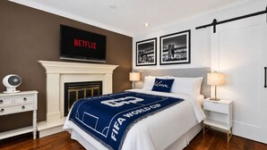A bedroom with a bed, a fireplace, a TV, and framed pictures on the wall. - Modern 6BR |Near Downtown| Fast WiFi| Free Parking (Vancouver)