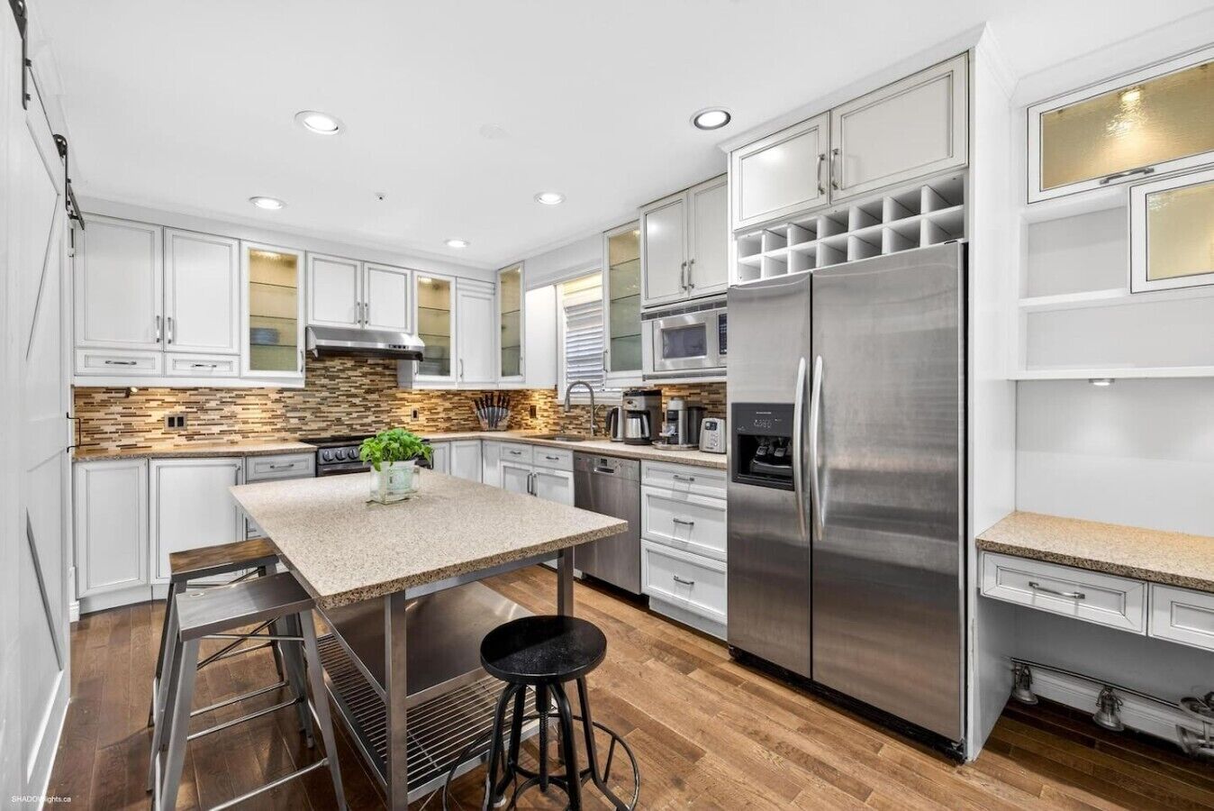 A modern kitchen with white cabinets, a stainless steel refrigerator, a built-in microwave, and a granite countertop.