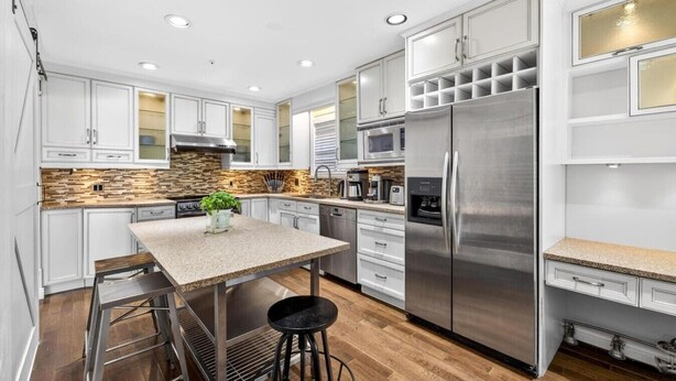 A modern kitchen with white cabinets, a stainless steel refrigerator, a built-in microwave, and a granite countertop. - Modern 6BR |Near Downtown| Fast WiFi| Free Parking (Vancouver)