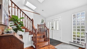A staircase with wooden railings, a door with glass panels, and a large window with a view of greenery. - Modern 6BR |Near Downtown| Fast WiFi| Free Parking (Vancouver)