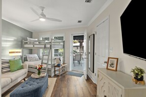Ein Zimmer mit Etagenbett, einer Couch, einem Couchtisch mit Blumen, einem Deckenventilator und einer Tür zu einem Außenbereich.