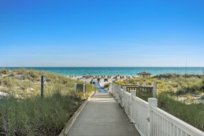 En træpromenade der fører til en strand med en pavillon og strandstole.