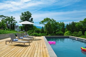 Una terraza de madera con sillas reclinables y una piscina.