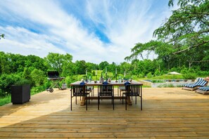 Une terrasse en bois avec une table dressée pour le repas, entourée de chaises, et un barbecue.
