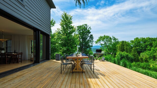 A wooden deck with a dining table and chairs, a grill, and a view of greenery and a house. - Pool + Deck Dining + BBQ | Kayaks + EV Charger • Catskills View | River View (Germantown)