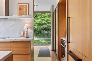Une cuisine moderne dotée de plans de travail en marbre, de meubles en bois, d’une cuisinière intégrée et offrant une vue sur un jardin verdoyant.
