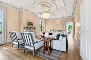Un salon avec une cheminée, un canapé, deux fauteuils, une table basse et une lampe.