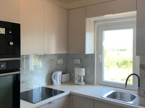 A modern kitchen with a built-in oven, a stovetop, a coffee maker, and a window providing a view of greenery.
