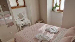 A bedroom with a bed, a dresser, a mirror, a small round table, and a window with a plant. - Diocletian Lux Apartment (Split)