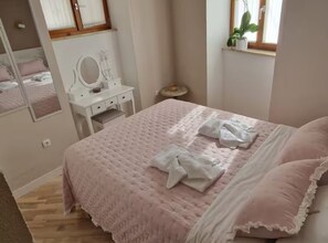 A bedroom with a bed, a dresser, a mirror, a small round table, and a window with a plant. - Diocletian Lux Apartment (Split)