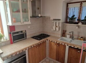 A compact kitchen with a microwave, stove, sink, and wooden cabinets. - Diocletian Lux Apartment (Split)