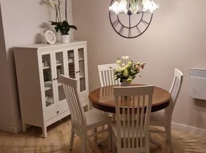 A dining area with a round table, white chairs, a cabinet with glass doors, and a wall-mounted clock. - Diocletian Lux Apartment (Split)