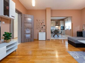 A modern living room with a wooden floor, a sofa, a TV, a plant, and a wall with motivational quotes.