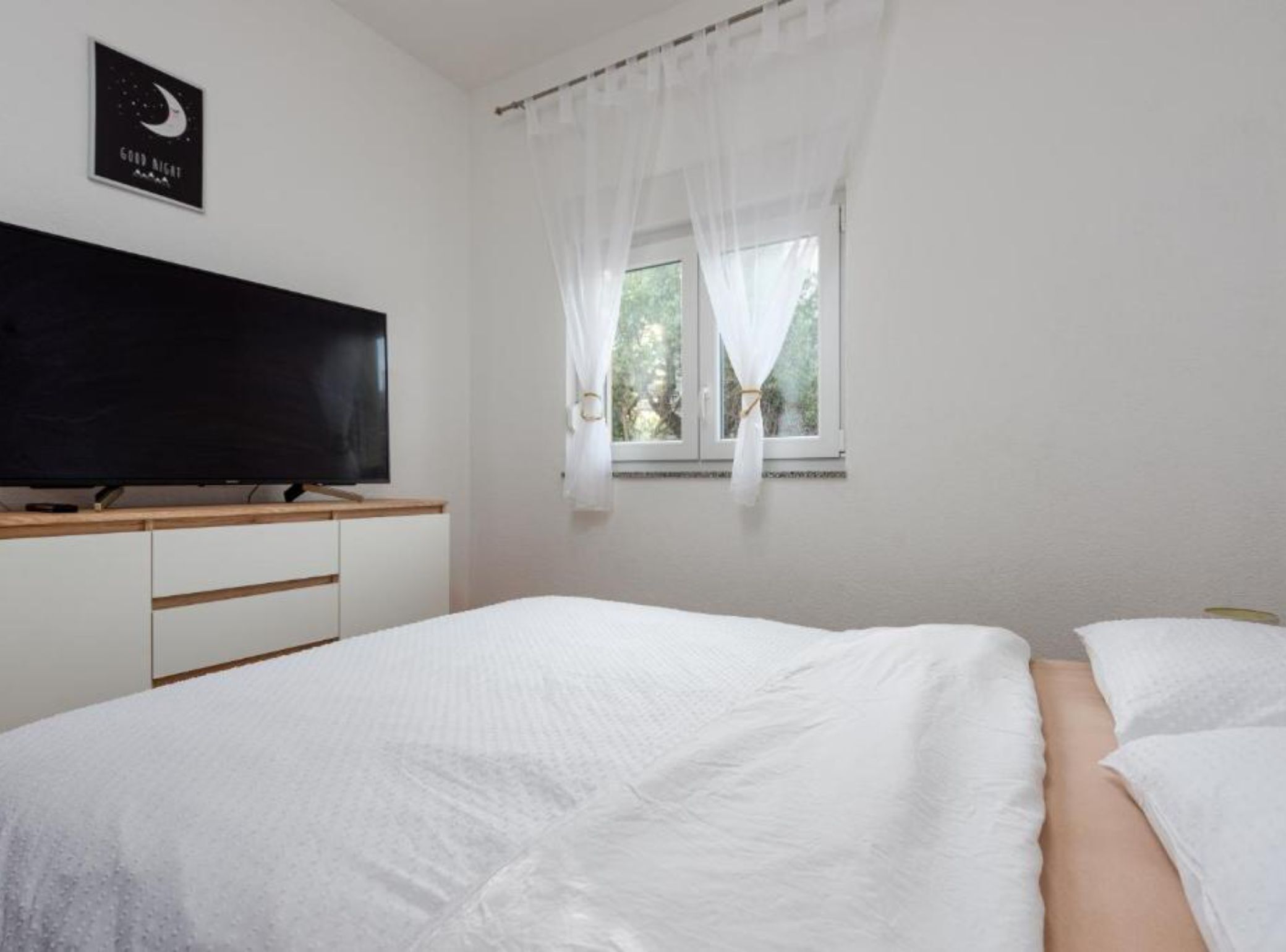 Une chambre à coucher avec un lit, une télévision, une fenêtre avec des rideaux et un panneau accroché au mur.