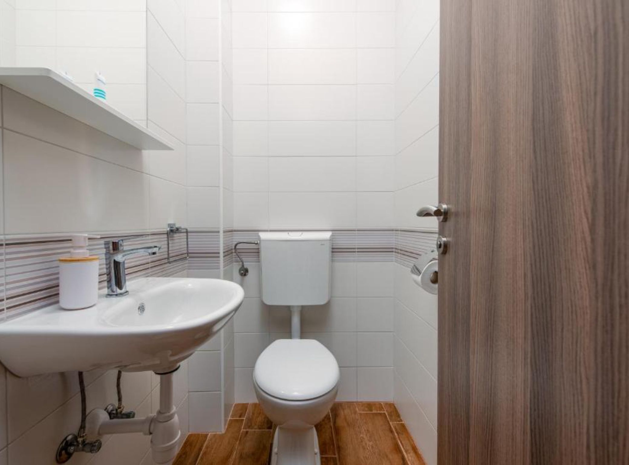 Une salle de bain avec un lavabo blanc, des toilettes et des carreaux de sol en bois.