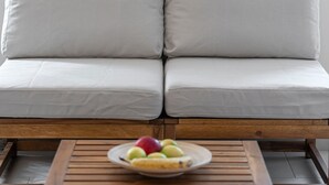 Un canapé avec des coussins, une table basse en bois sur laquelle se trouve un panier de fruits, et un plancher en bois.