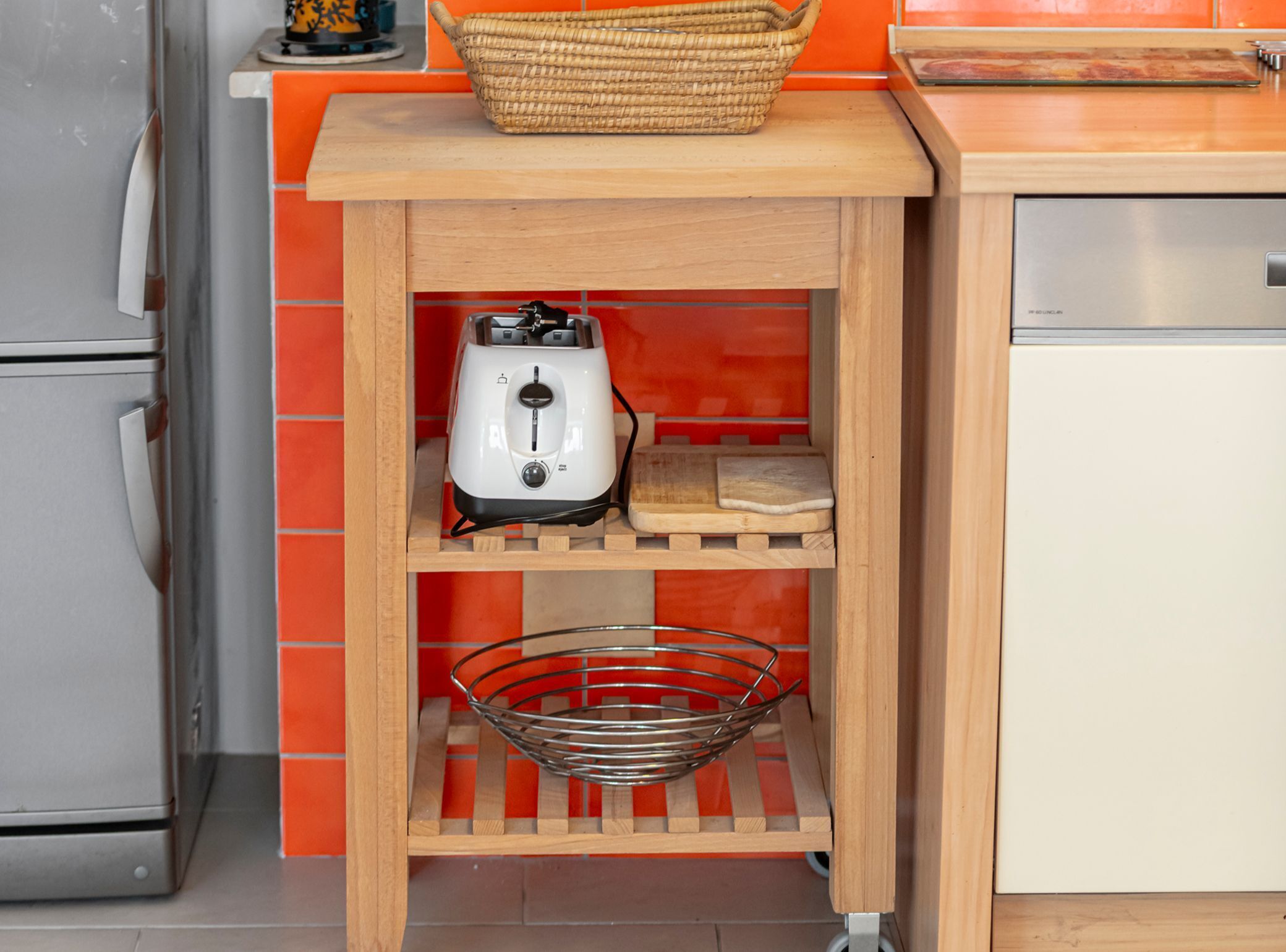 Une cuisine avec un grille-pain posé sur une étagère en bois, un panier sur le dessus et une passoire en métal sur une étagère inférieure.
