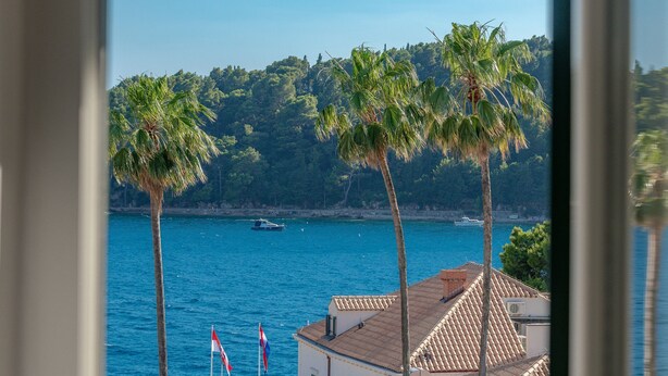 Une vue sur la côte, avec des palmiers, une mer bleue et limpide, et des bâtiments aux toits de tuiles.