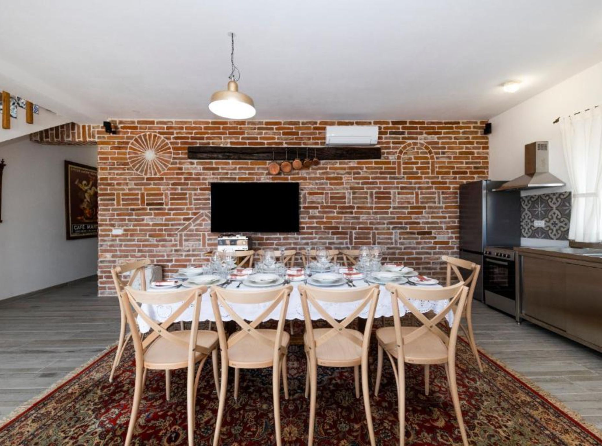 A dining area with a brick wall, a flat-screen TV, and a modern kitchen in the background.