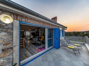 Ein Gebäude aus Stein mit einem Balkon, einer Schiebetür aus Glas und Außenmöbeln.