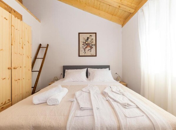 Un dormitorio con cama, ropa de cama blanca, una escalera de madera, un cuadro en la pared y un armario de madera.