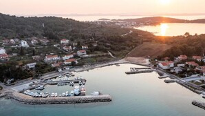 An aerial view of a coastal town with a marina, houses, and a sunset over the water.