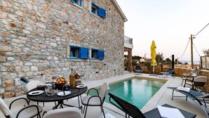A stone building with a pool, outdoor seating, and a yellow umbrella.