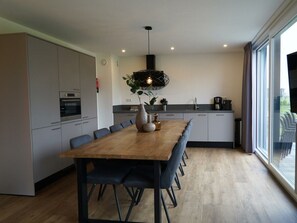 Een moderne keuken met een eethoek, met een houten tafel, zwarte stoelen en een hanglamp.
